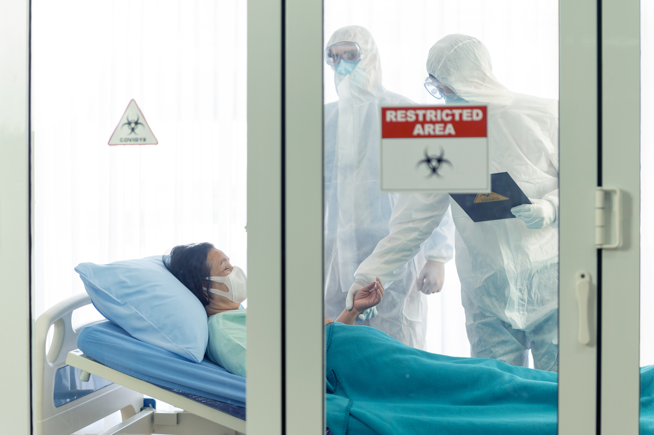 Two doctors in hazmat suits treating a COVID patient in isolation