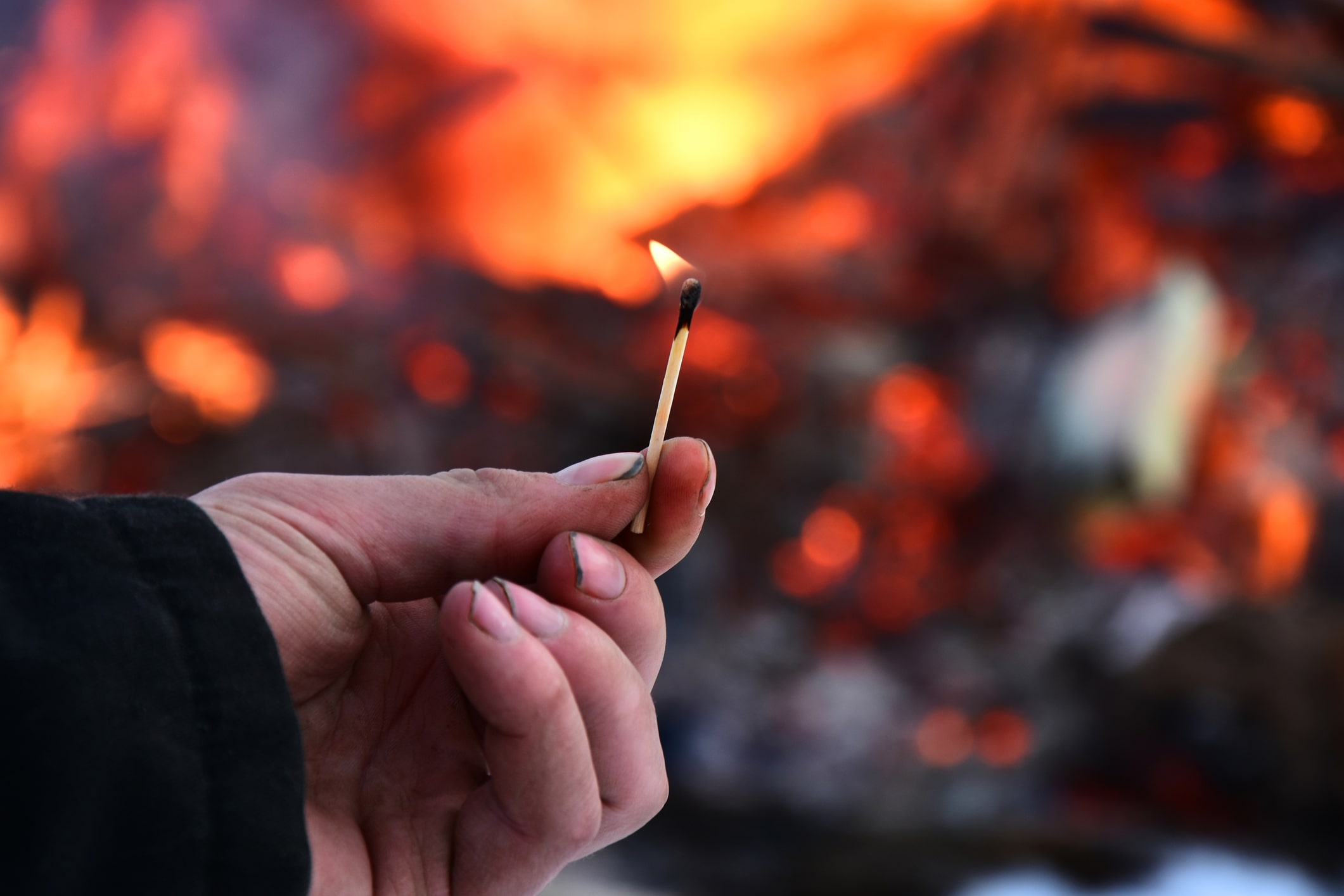 Burning match in front of a large fire