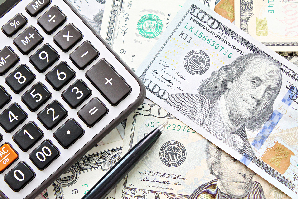 Top-down view of a calculator and pen on top of dollar bills